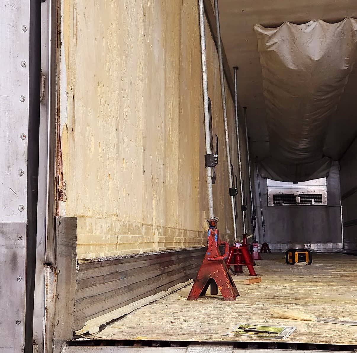 Jack stands and load bars propping up a trailer wall and roof during a repair
